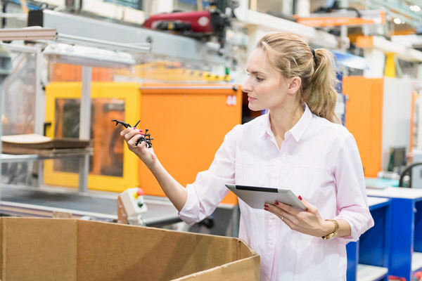 Horizontal color image of woman working at modern plastic factory and holding digital tablet and examining quality of plastic merchandise.